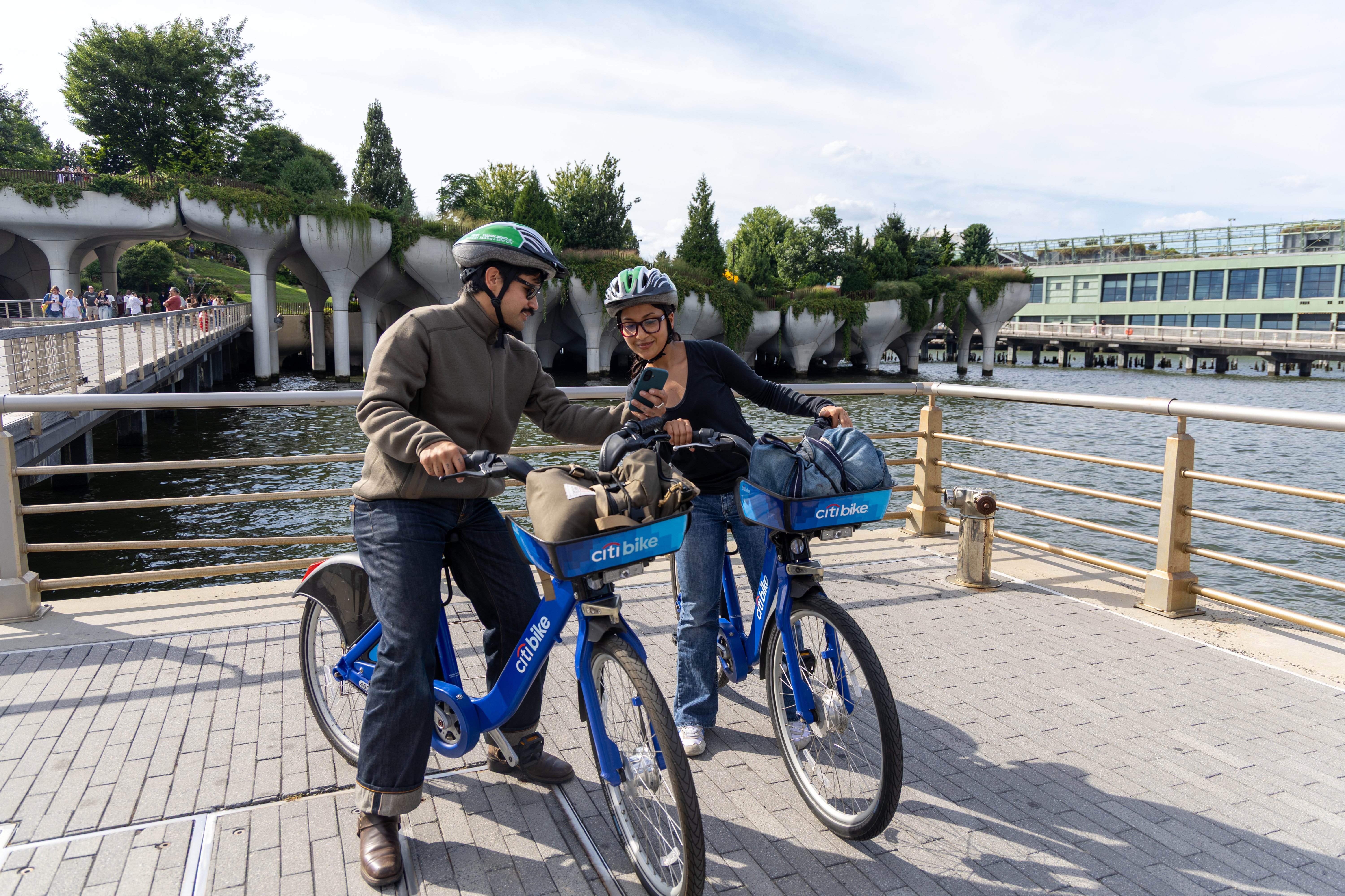 A man shows a woman something on his smartphone while both are sitting on Citi Bikes.